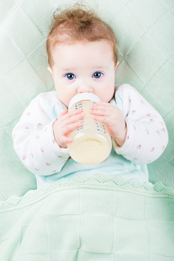 Beautiful little baby with a milk bottle under a warm knitted blanket